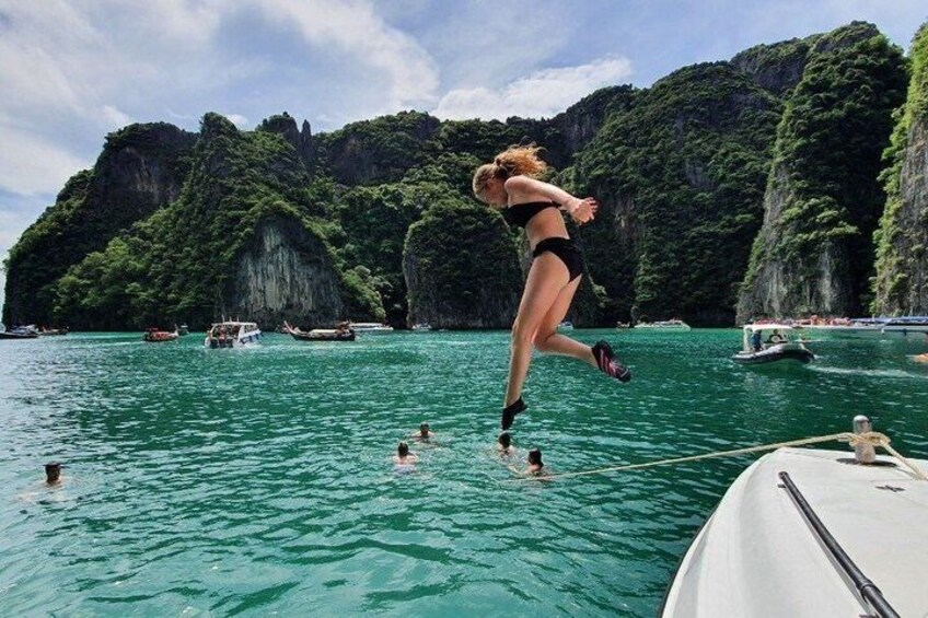 A woman jumping into the water from a boat, surrounded by lush green cliffs and other boats. 5