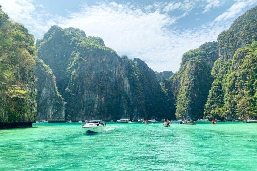 A turquoise sea with boats, surrounded by lush green cliffs. 2