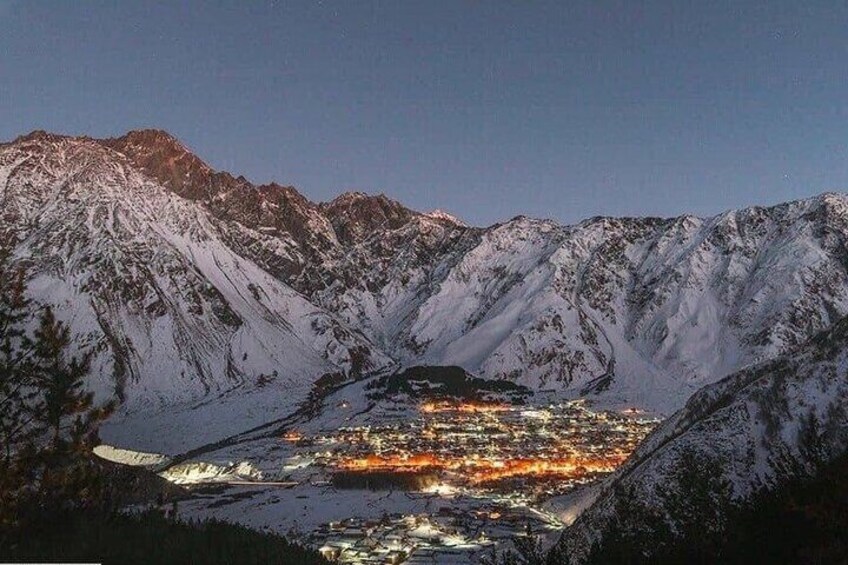 A snow-covered mountain range with a town illuminated in the valley below. 1
