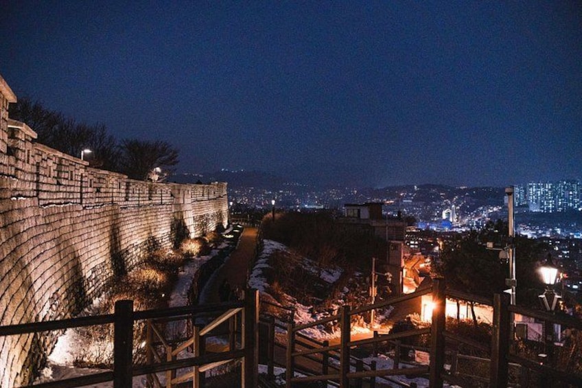 Un muro de piedra, una escalera y un paisaje urbano nocturno. 2