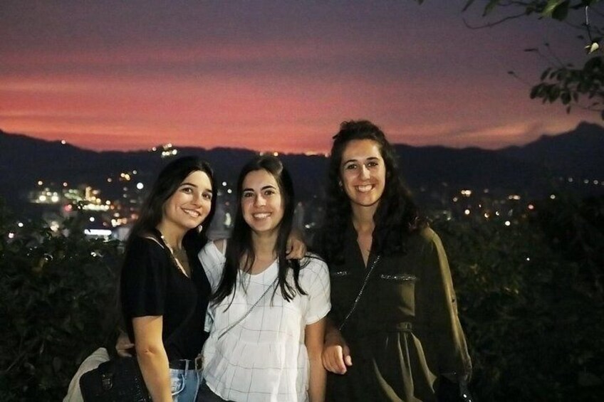 Trois personnes se tiennent à l’extérieur, au crépuscule, avec une vue sur la ville en arrière-plan. 2