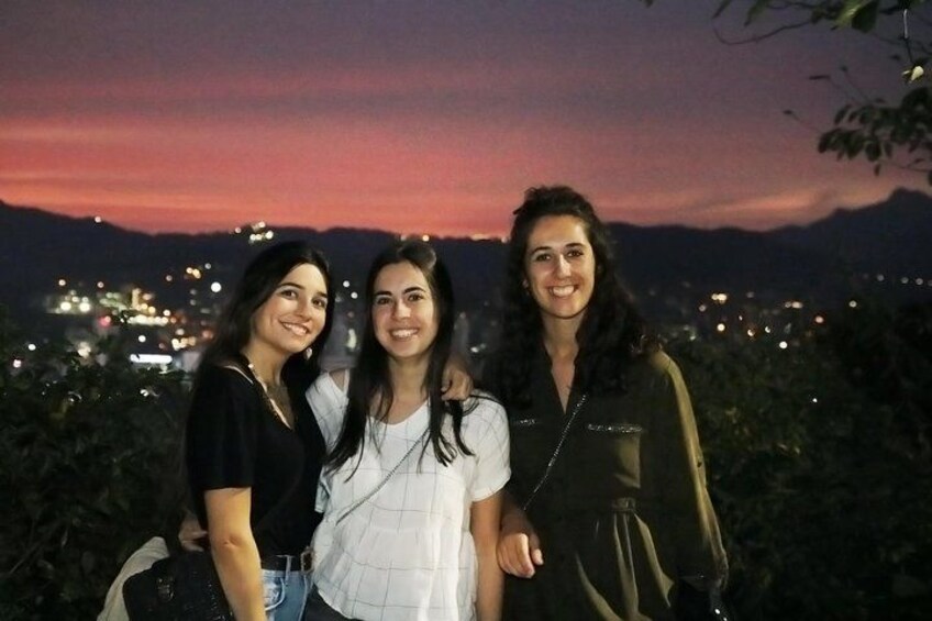 Three individuals standing outdoors with a cityscape and mountains in the background. 2
