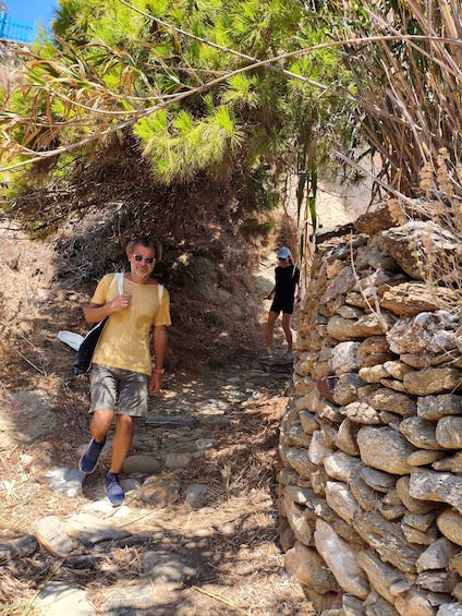 Una persona caminando por un sendero de piedra rodeado de vegetación seca y un muro de piedra. 5