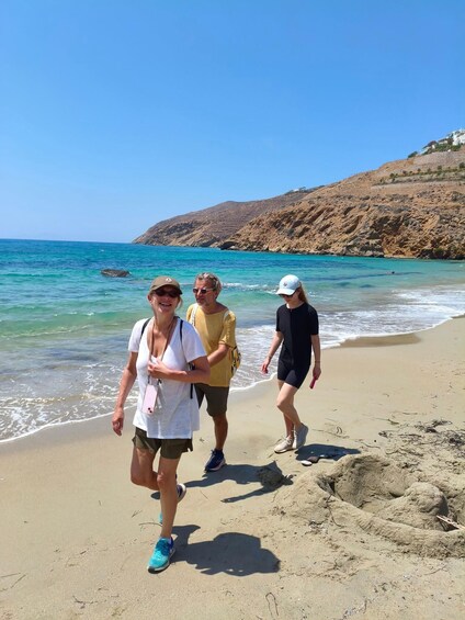 Tres personas caminando sobre una playa arenosa con agua azul cristalina y una ladera rocosa al fondo. 4