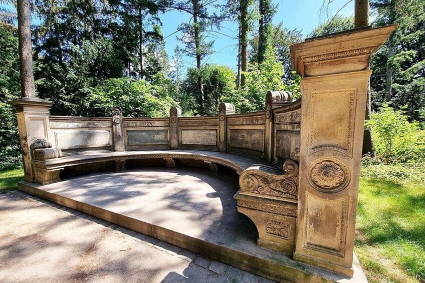 A stone bench with ornate carvings in a park. 5