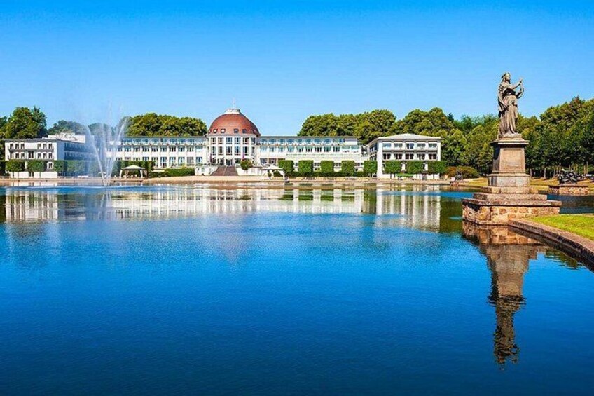 A calm lake with a fountain, a statue, and a building with a dome. 1