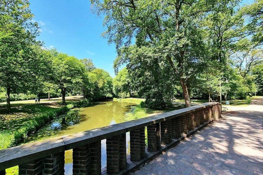 A park with a brick bridge over a calm river, surrounded by lush green trees. 4