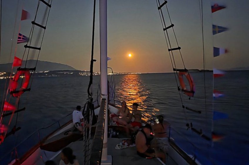 A sunset on the water with a sailboat and people on deck. 2