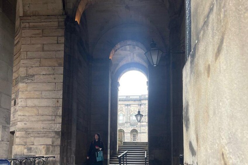 A stone archway with a person standing in the foreground and a building in the background. 2