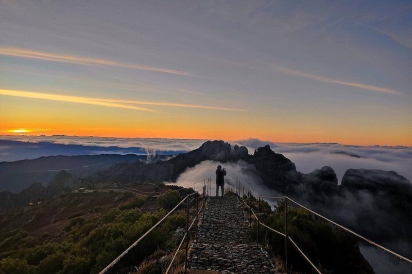 A person standing on a stone staircase overlooking a misty landscape with a sunset in the background. 1