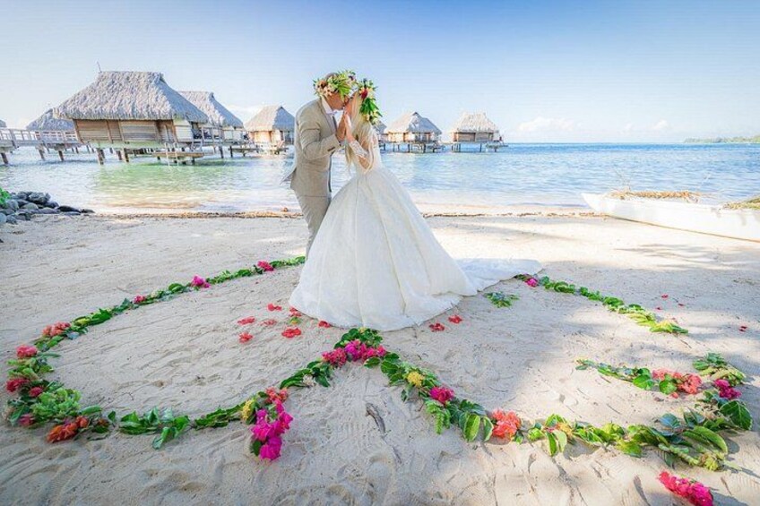 A couple kissing on a beach with overwater bungalows in the background. 4