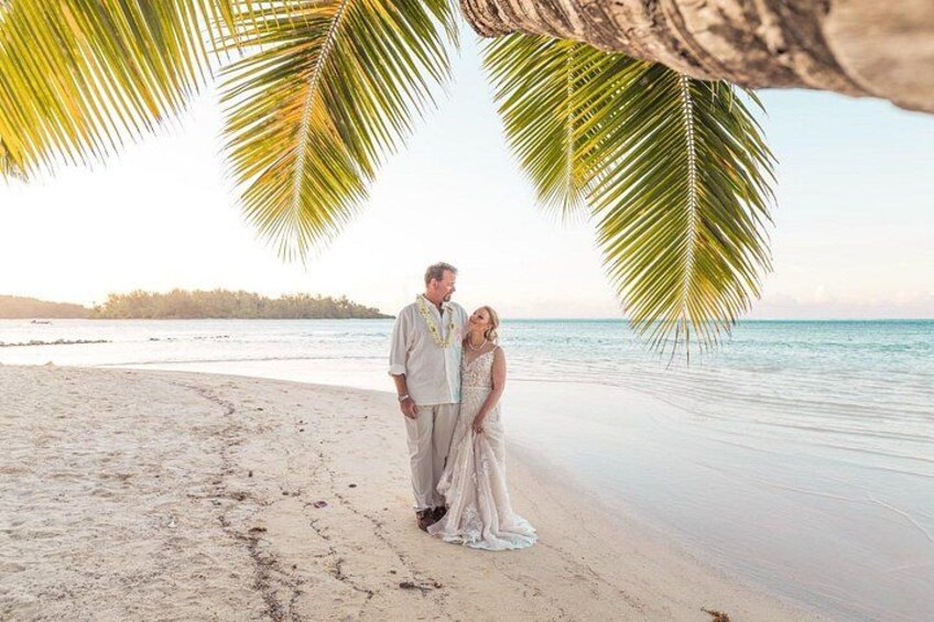 A couple on a beach with palm trees and a calm sea in the background. 2