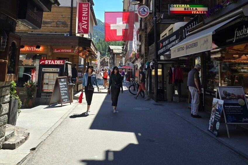 A street with shops, a Swiss flag, and people walking. 2