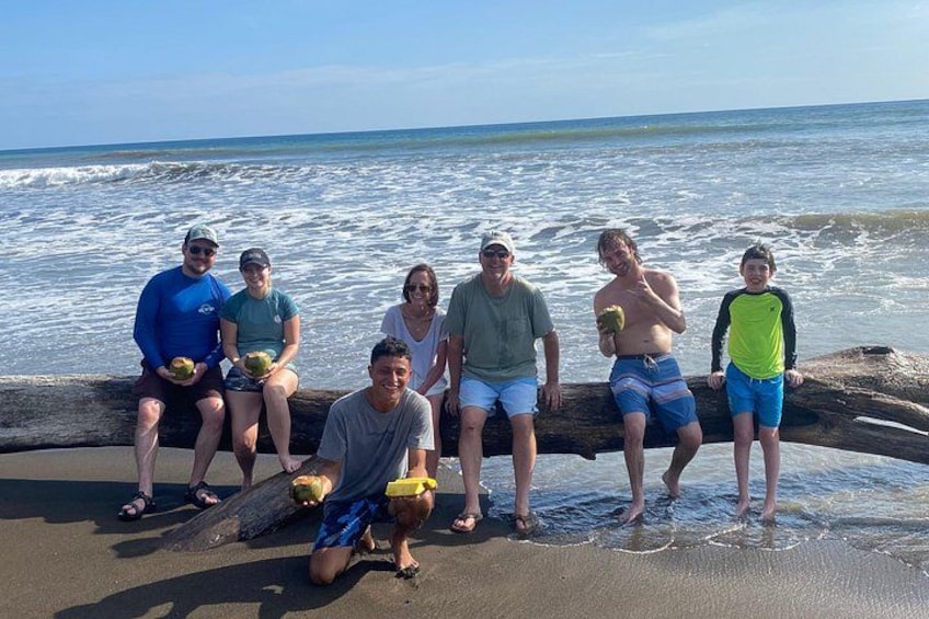 A group of people sitting and standing on a beach with the ocean in the background. 2