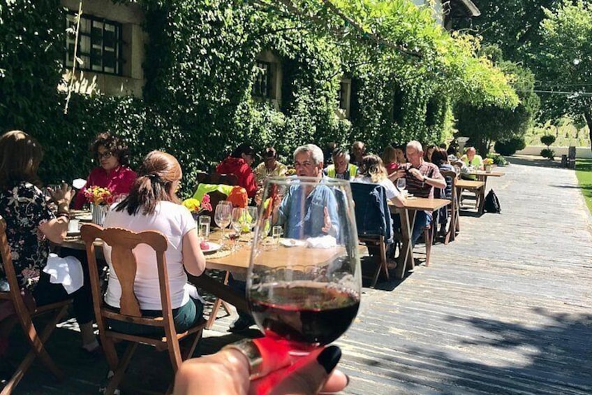 People dining outdoors at wooden tables, surrounded by greenery. 1