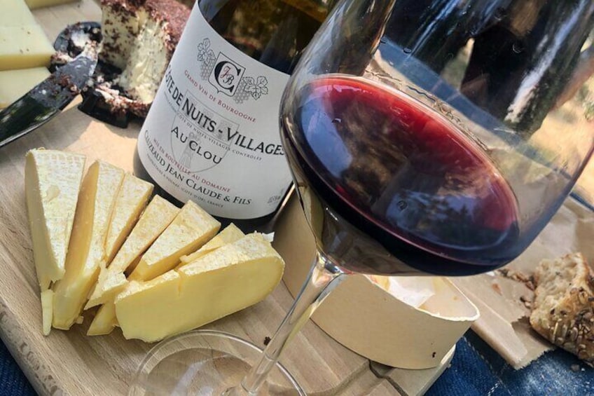 Una botella de vino tinto, una copa de vino tinto y rebanadas de queso sobre una tabla de madera. 4