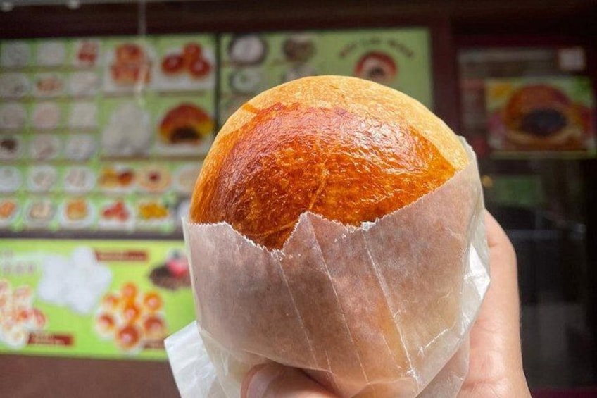 A hand holding a bread roll with a shiny crust, in front of a menu board with various food items. 3
