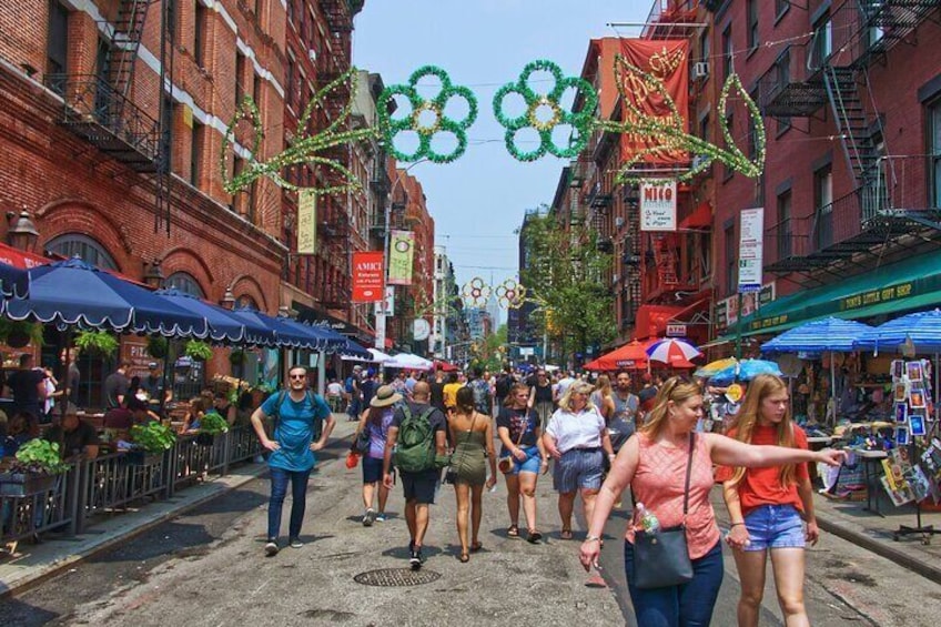 A busy street lined with brick buildings, outdoor cafes, and festive decorations. 3