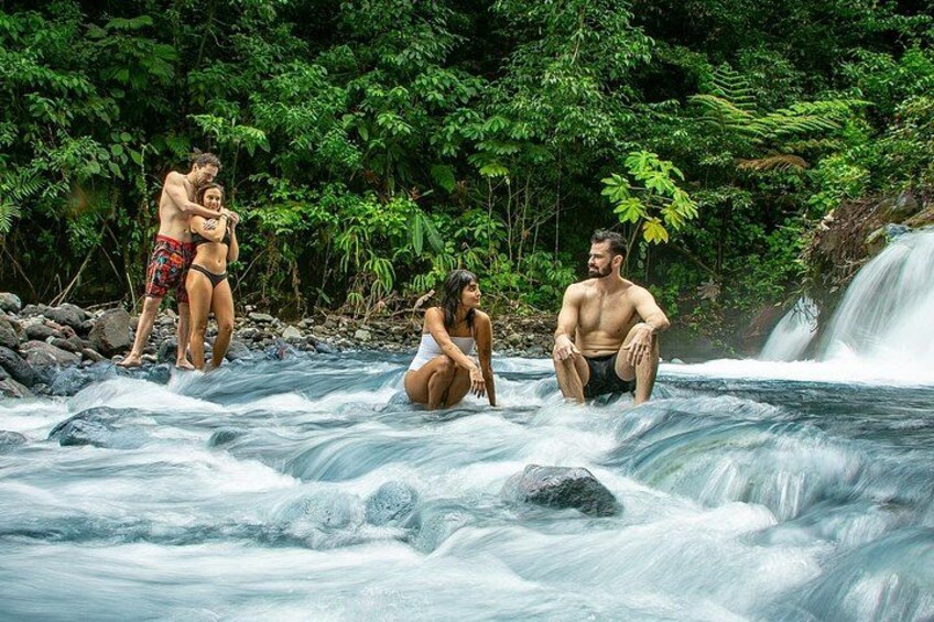 Une rivière où des personnes se tiennent debout et sont assises dans l'eau, entourées d'une végétation luxuriante. 5