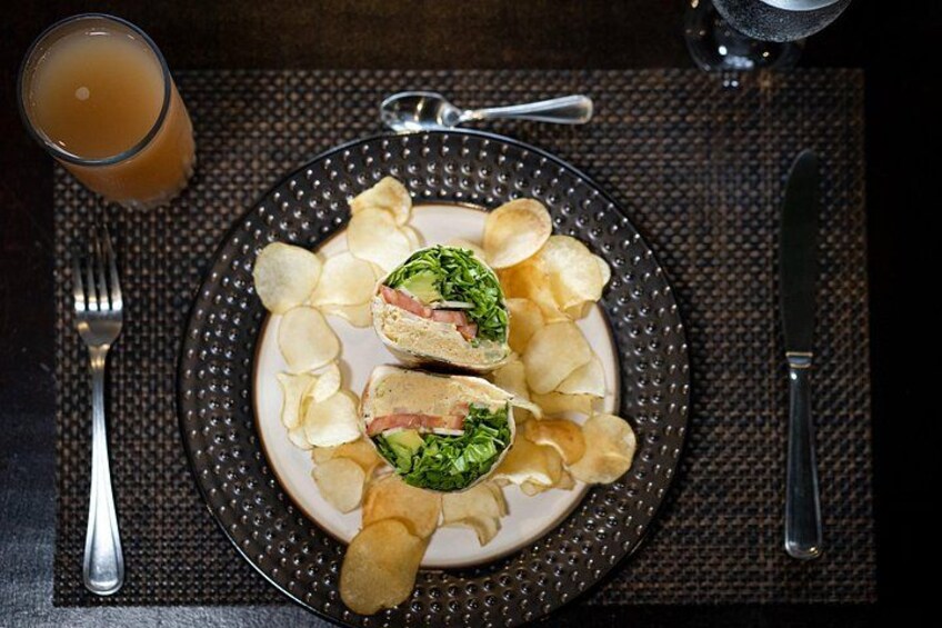 Une assiette contenant un sandwich coupé en deux, des chips et un verre de jus d’orange, le tout posé sur une table. 4