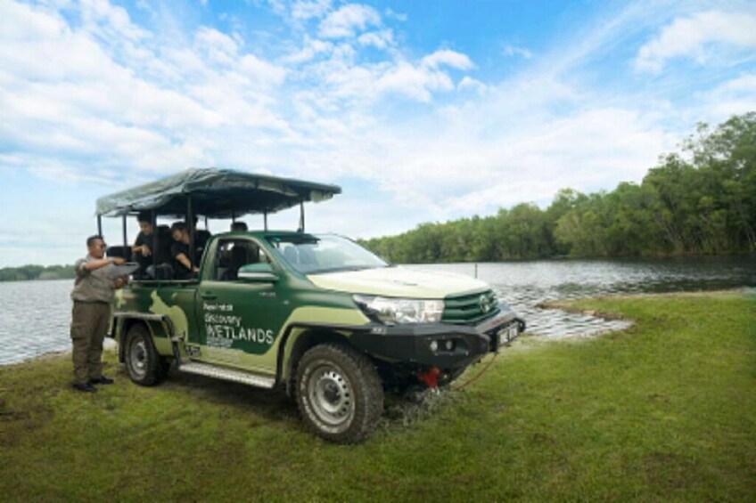 Een groene Discovery Wetlands-voertuig geparkeerd bij een meer, met mensen binnen. 3