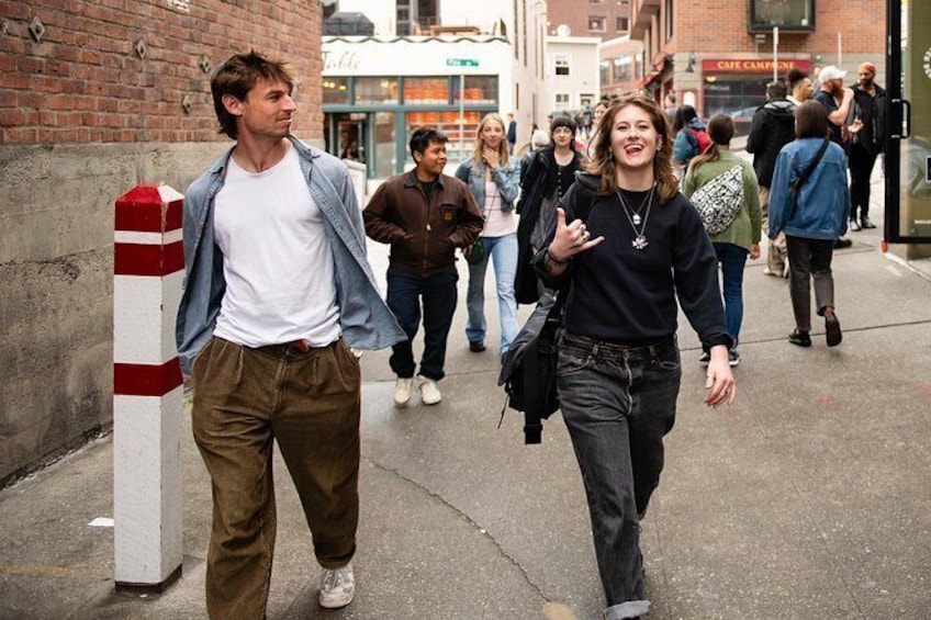 Two people walking on a sidewalk, a brick wall, and a red and white striped post. 2
