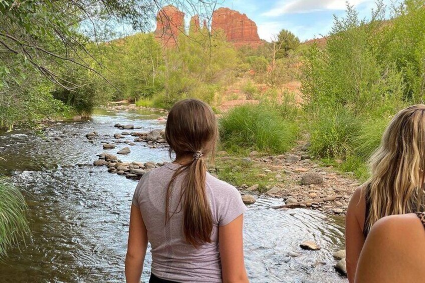 A river with rocks and greenery, with a red rock formation in the background. 1