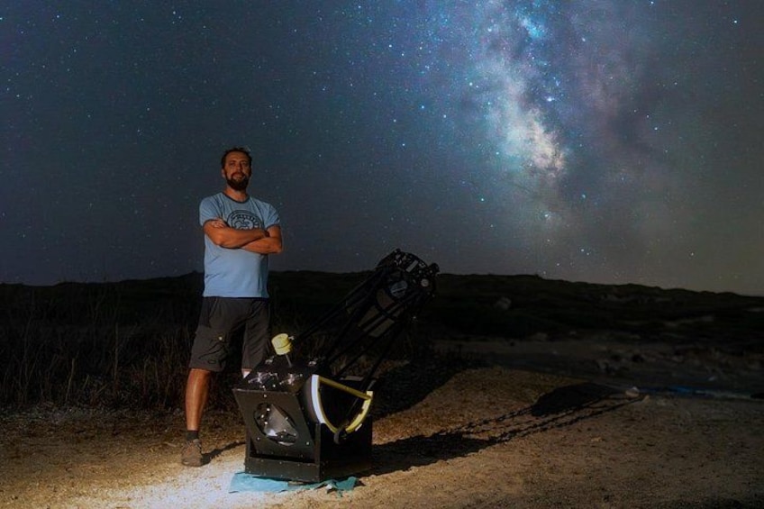 A person standing next to a telescope on a sandy ground with a starry sky in the background. 3