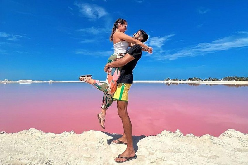 A person carrying another on their shoulders on a beach with a pinkish water body in the background. 1
