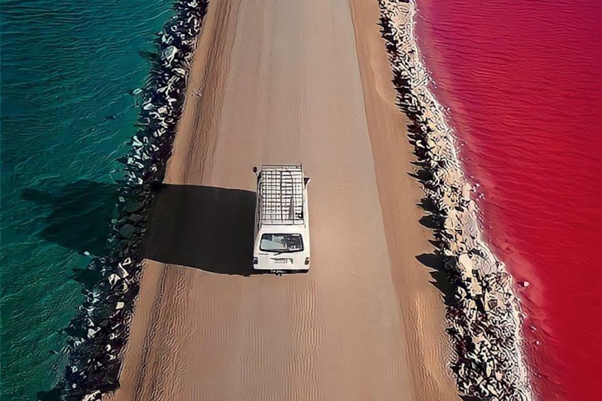 A white vehicle parked on a narrow road between two bodies of water with different colors. 2