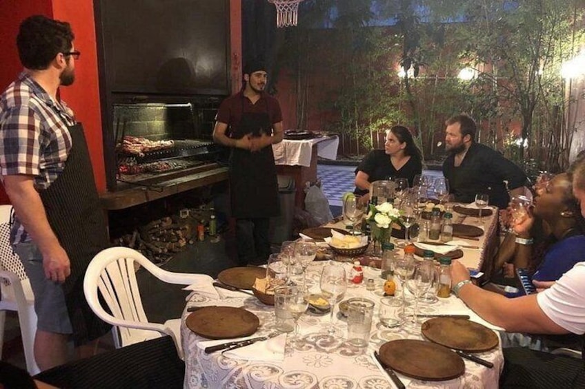 A group of people dining outdoors at night with a grill and table set with plates, glasses, and cutlery. 5