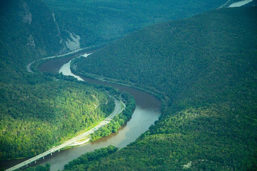 A river winding through a forested valley with a bridge crossing over it. 1