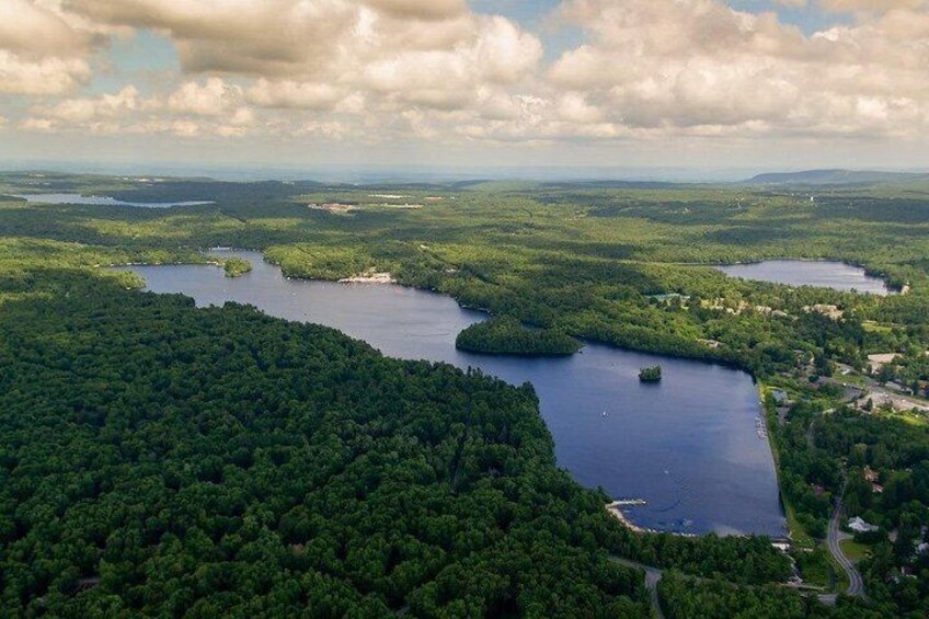 Un lago rodeado de bosque denso, con una carretera y edificios a lo lejos. 3