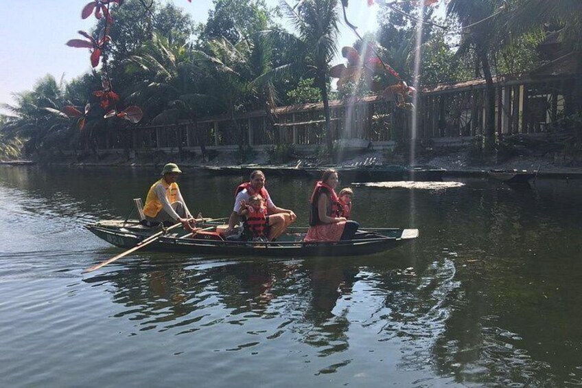 A group of people in a small boat on a calm river, surrounded by lush greenery and a wooden structure in the background. 3