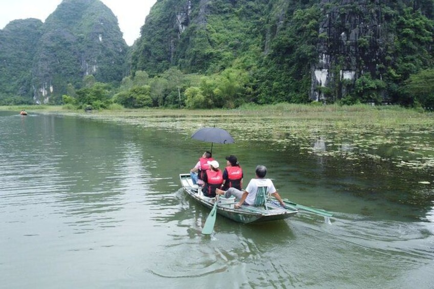 A boat with three people on a calm river surrounded by lush greenery and tall cliffs. 2