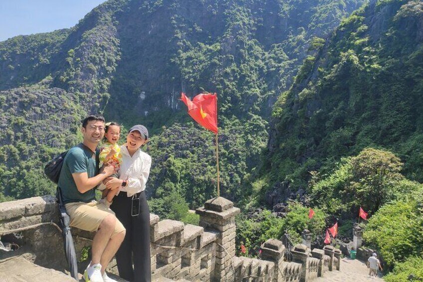 Una persona sosteniendo a un niño, una bandera roja, y un muro de piedra con un paisaje montañoso al fondo. 5