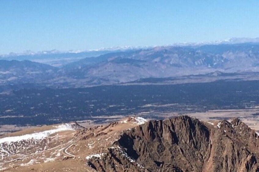 Eine gebirgige Landschaft mit Schneeflecken, felsigem Gelände und weit entfernten, schneebedeckten Bergen. 2