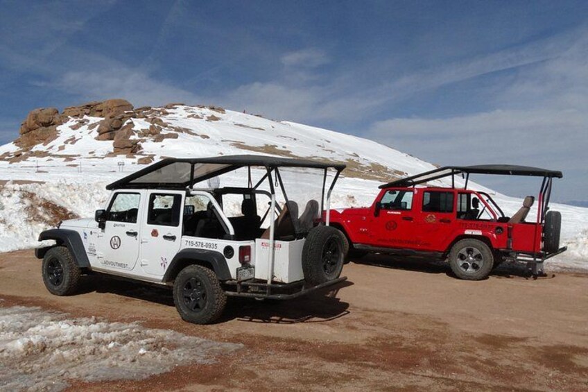 Two off-road vehicles parked on a dirt road with snow-covered hills in the background. 1