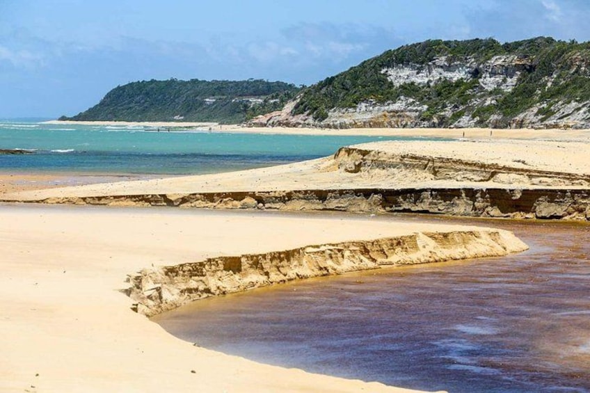 A beach with clear water, a sandy shore, and a rocky outcrop in the background. 5