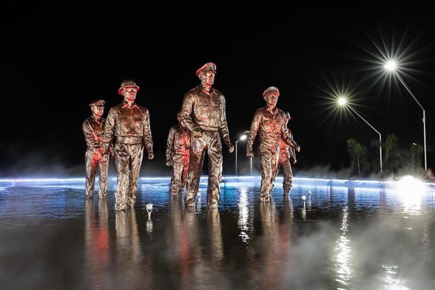 Escena nocturna con estatuas de soldados en el agua, iluminadas por farolas. 1