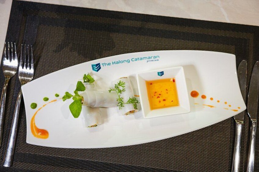 Un plato blanco con un elemento blanco enrollado, un recipiente cuadrado pequeño con salsa amarilla y guarnición verde. 3