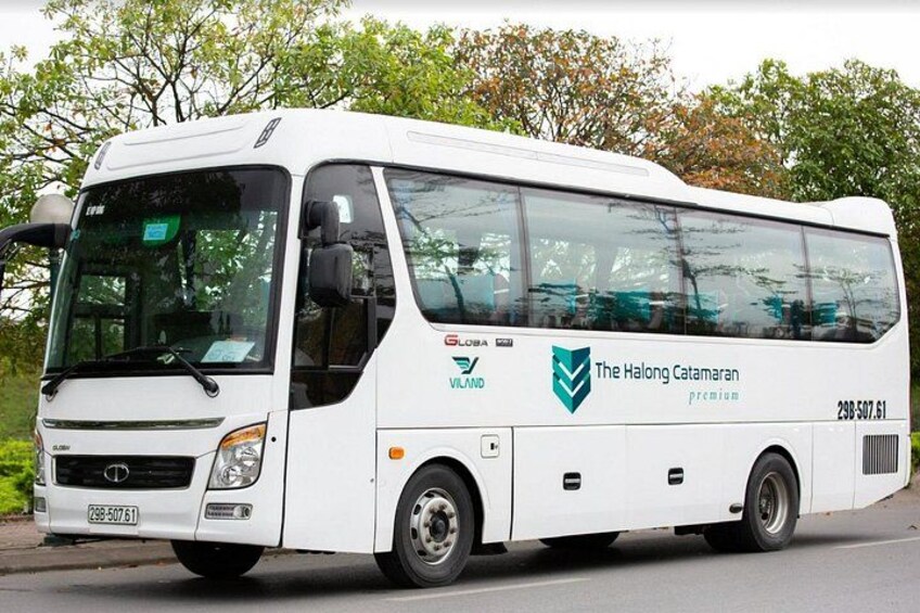 Un autobús blanco con la marca 'The Halong Catamaran', estacionado en una calle con árboles al fondo. 4