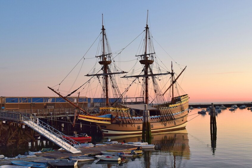 A large sailing ship docked at a pier with smaller boats nearby. 1