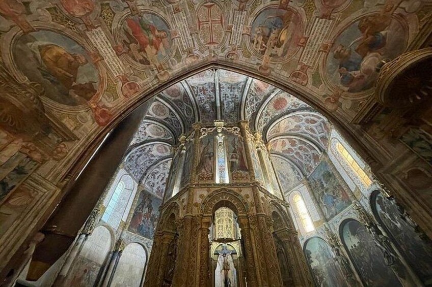 Interior de iglesia ornamentado con un alto techo abovedado, frescos detallados y un ventanal central de vidrieras. 4