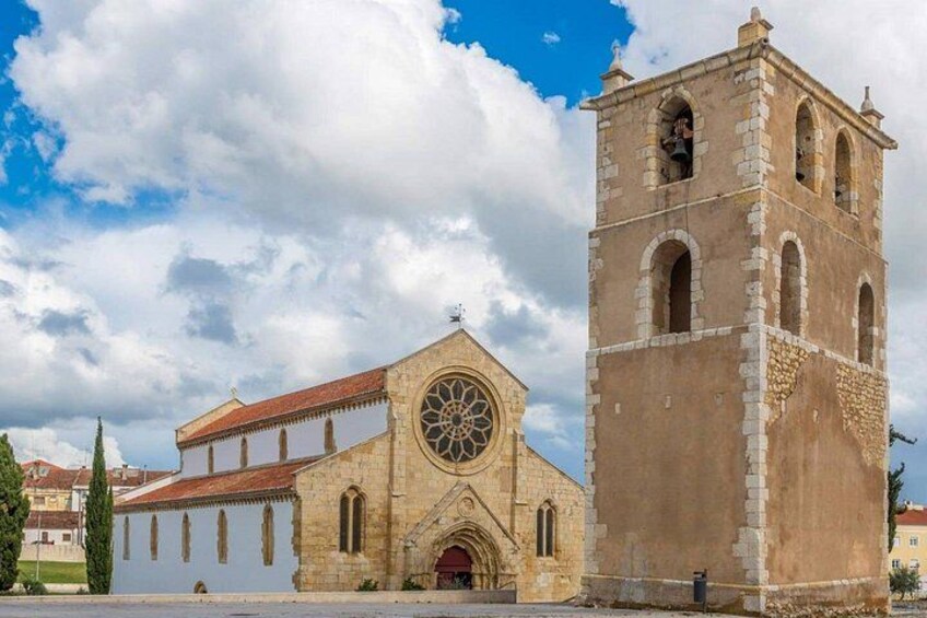 Una iglesia histórica con un campanario, un ventanal circular grande y un techo de tejas rojas. 2