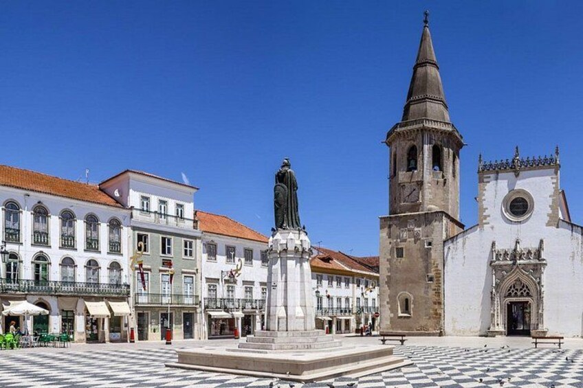 A plaza with a statue, a church with a bell tower, and historic buildings. 1