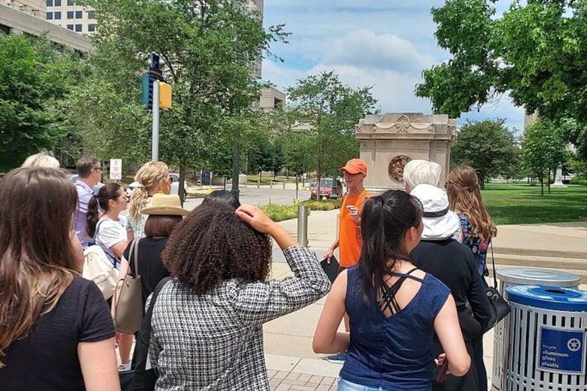 A group of people standing outdoors, a traffic light, and a monument. 5