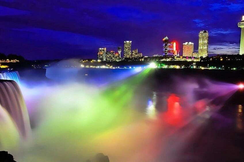 A city skyline at night with illuminated buildings and a waterfall. 2
