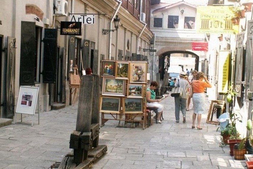 A street with art displays, a sign for 'Artei,' and people walking. 1