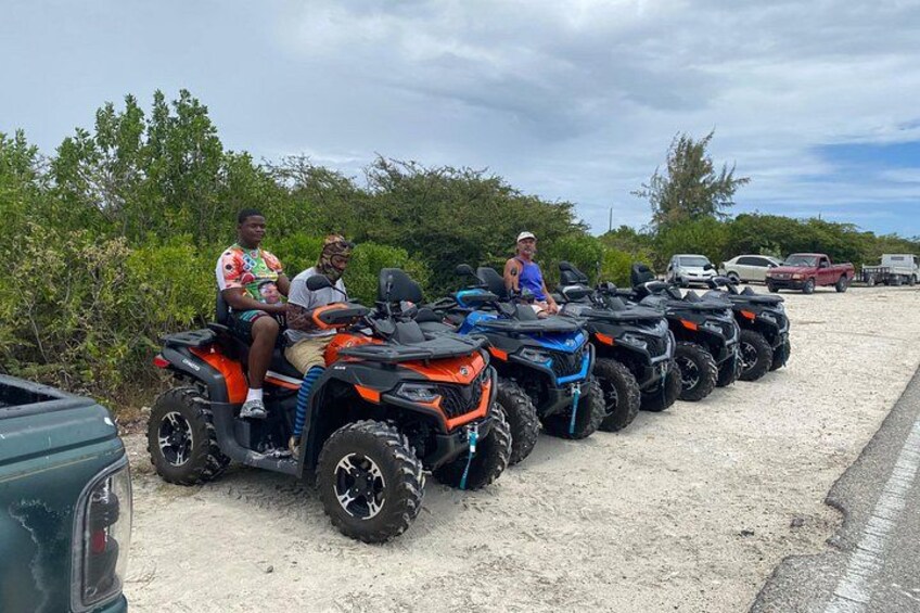 A row of ATVs parked on a sandy area with people sitting on them. 2